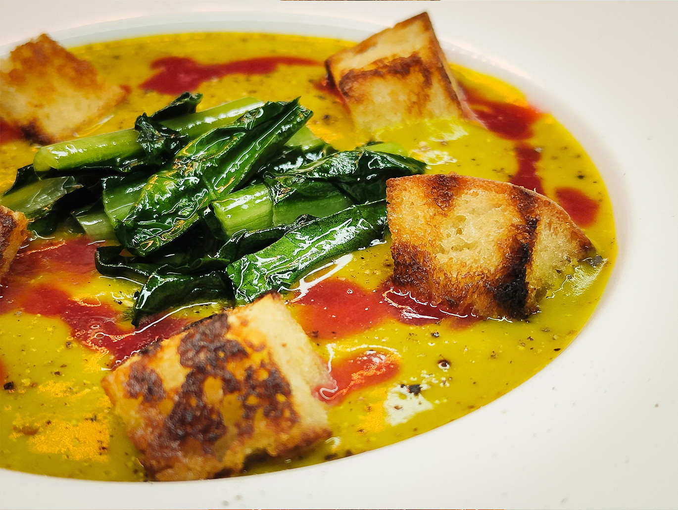 Vellutata di zucca con cicoria saltata, salsa di lamponi e pane croccante al burro